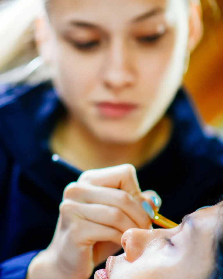 PMU training demonstration: blonde artist applying eyeliner.