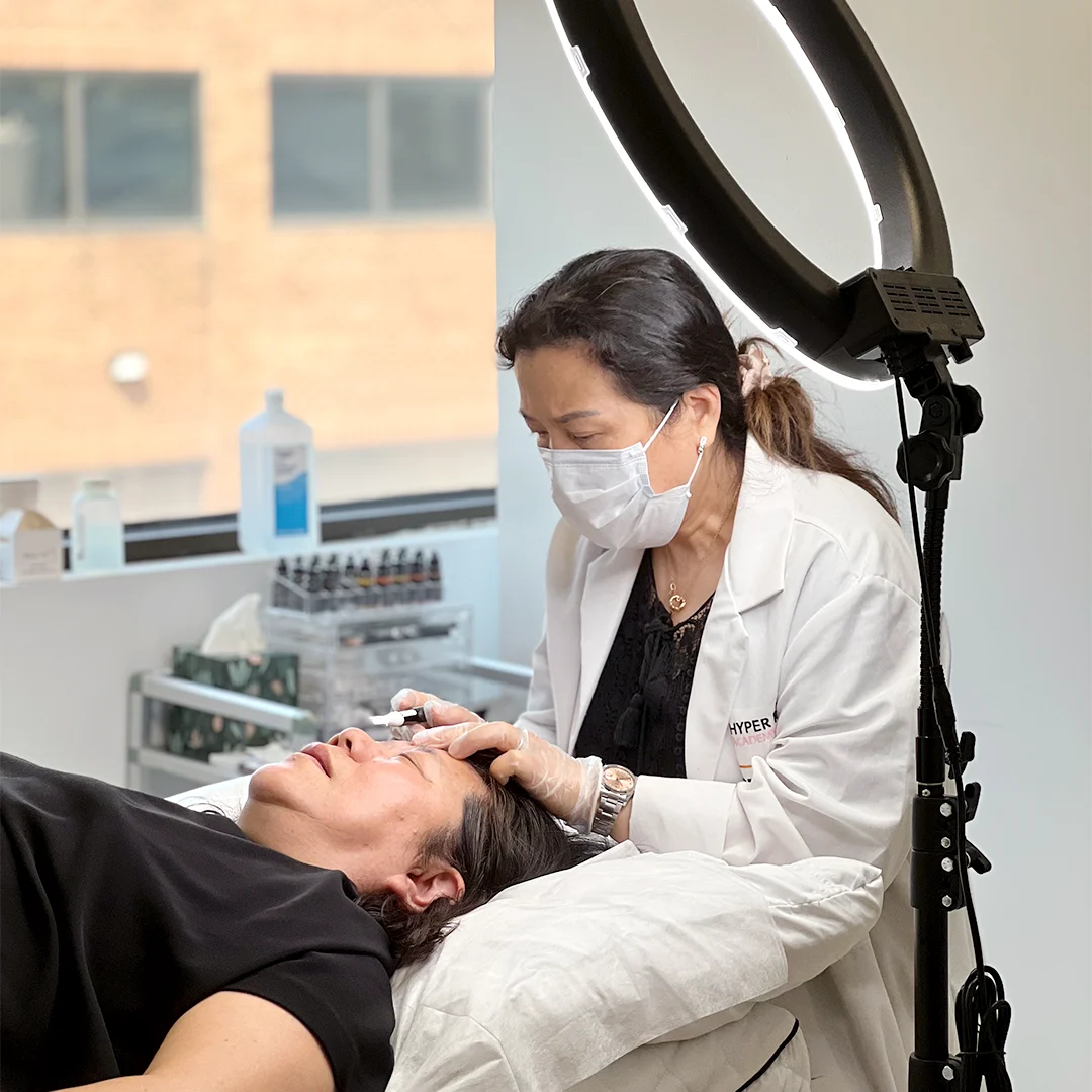 Hyper Real Academy PMU training. Technician demonstrating nano brows or hair strokes on a client using RealTint.