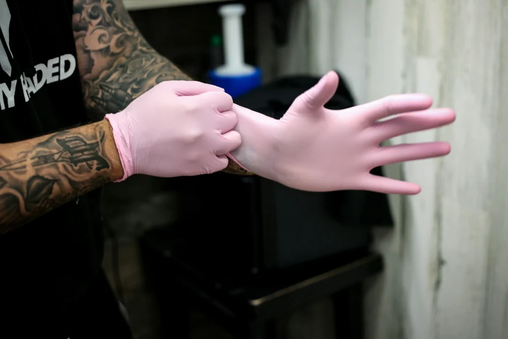 Tattooed PMU artist putting on pink gloves for permanent makeup training, SMP, or RealTint demonstration.