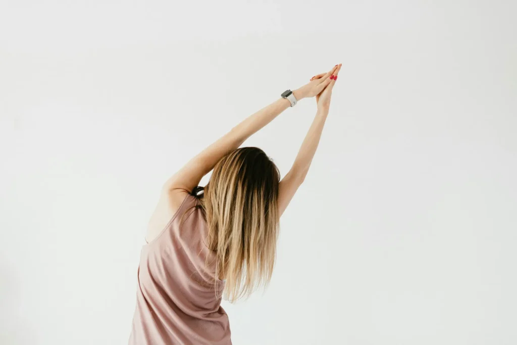 Woman with ombre hair stretching arms up in pink top, PMU training wellness.