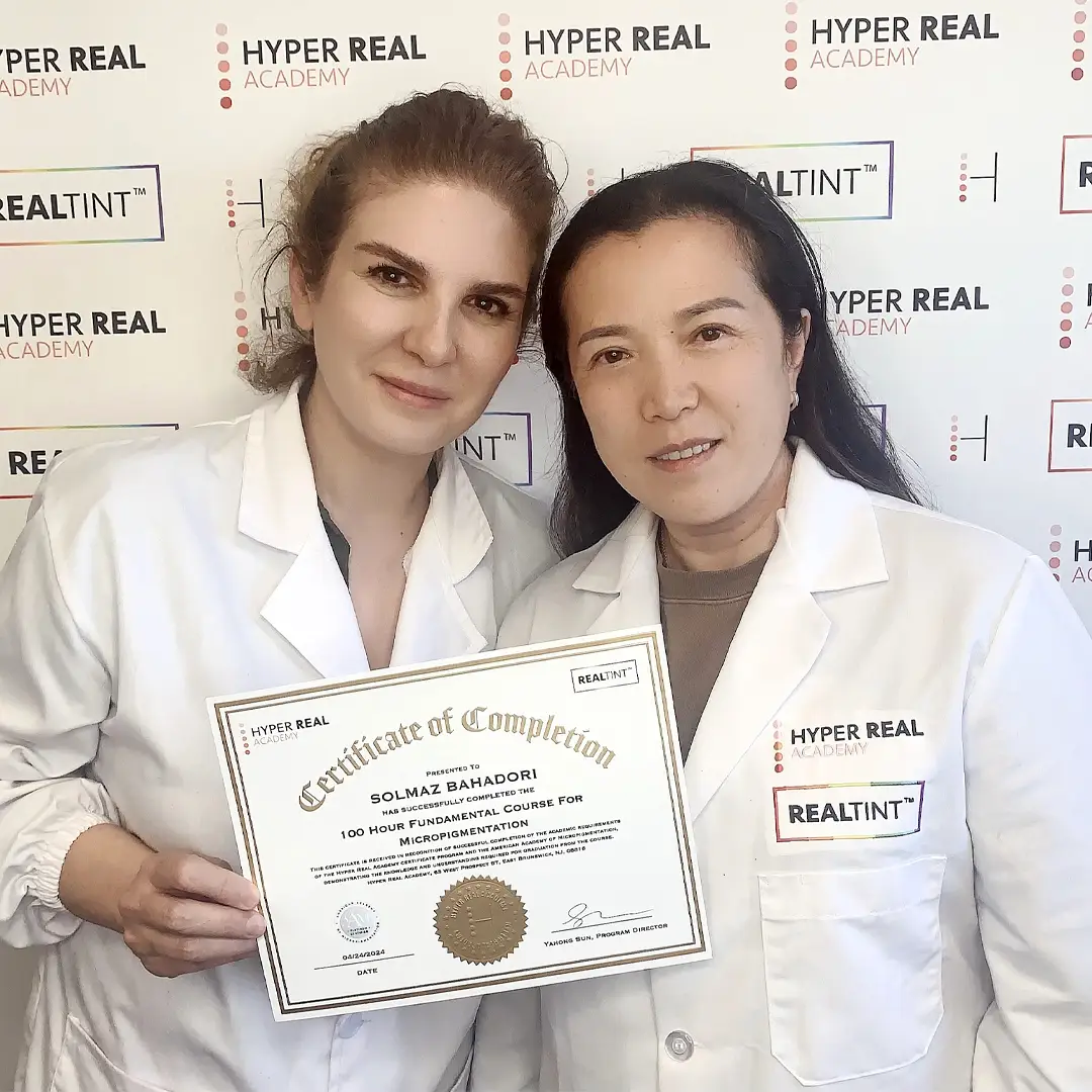 Graduate and program director hold a Certificate of Completion for the 100-Hour Fundamental Course for Micropigmentation