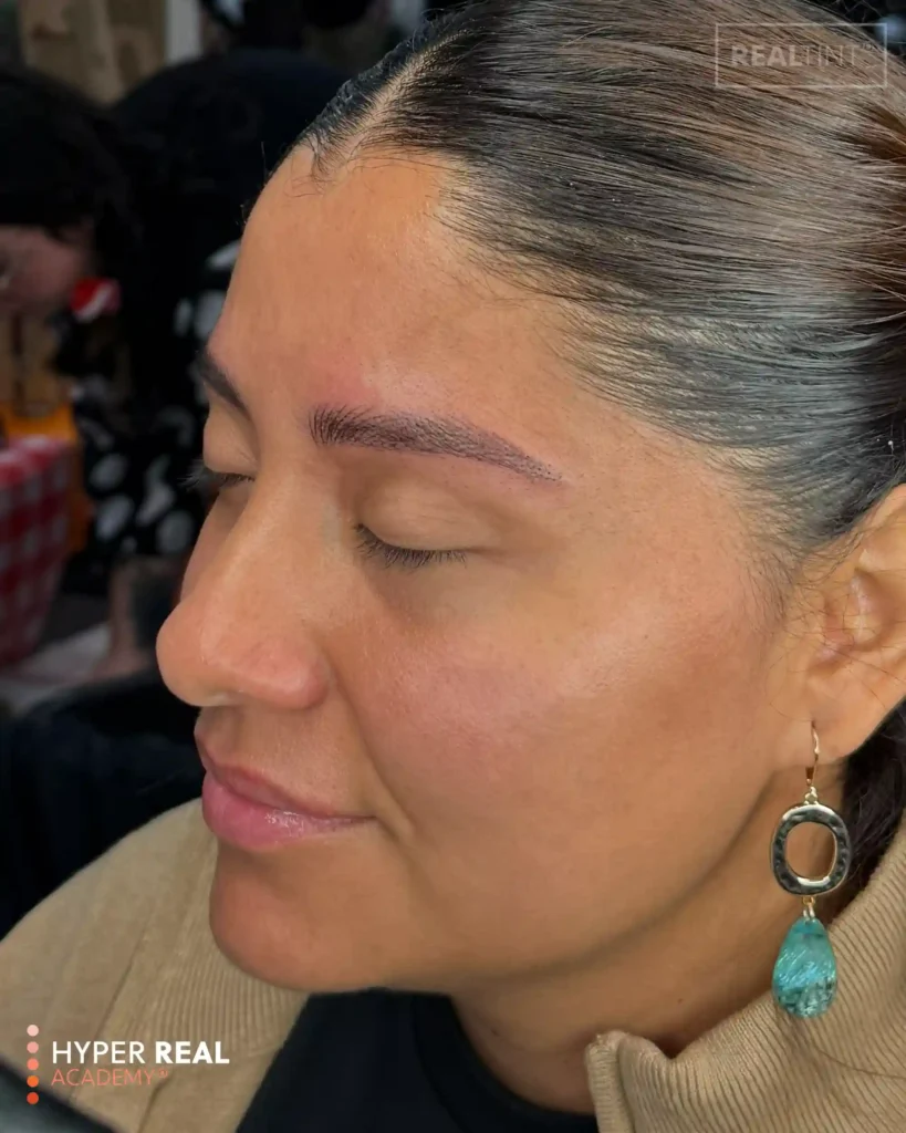 PMU eyebrow mapping phase. Technician's gloved hand drawing white pencil guidelines on client's forehead above natural brow. Faint white hair-stroke patterns visible. Hyper Real logo. Shows pre-procedure mapping for microblading or nano brows.