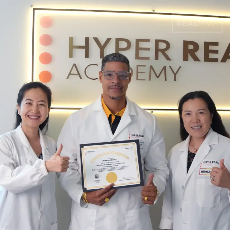 Hyper Real Academy instructor performing brow mapping for a PMU procedure. A professional in a white coat and pink mask uses a pencil to design eyebrows on a client, demonstrating techniques for nano brows, powder brows, and permanent makeup. RealTint® branding visible.