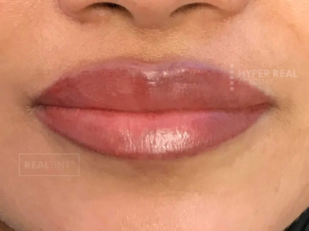 Lip blush mapping phase. Close-up of lips being outlined with black pencil. Thick dark border drawn around upper lip, pencil tracing lower lip. PMU preparation showing mapping technique for lip tattooing.