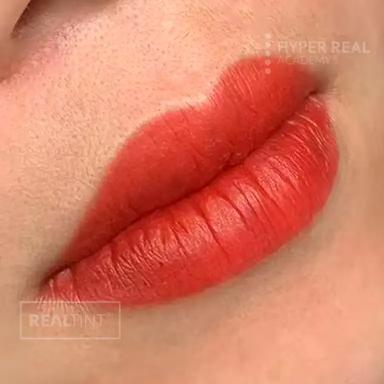 Lip blush PMU close-up with rosy-pink enhanced lips on medium-dark skin tone. Slight gloss from healing ointment. Watermarks 'HYPER REAL' and 'PERMANENT MAKEUP' visible.