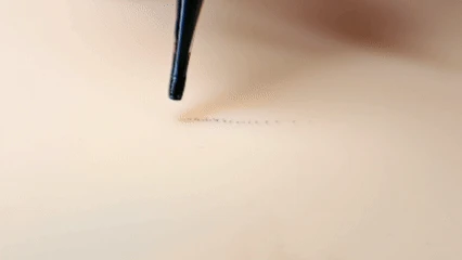 GIF of a fine needle tip laying a stippled dotted line on synthetic training skin, demonstrating soft-focus dotwork shading technique