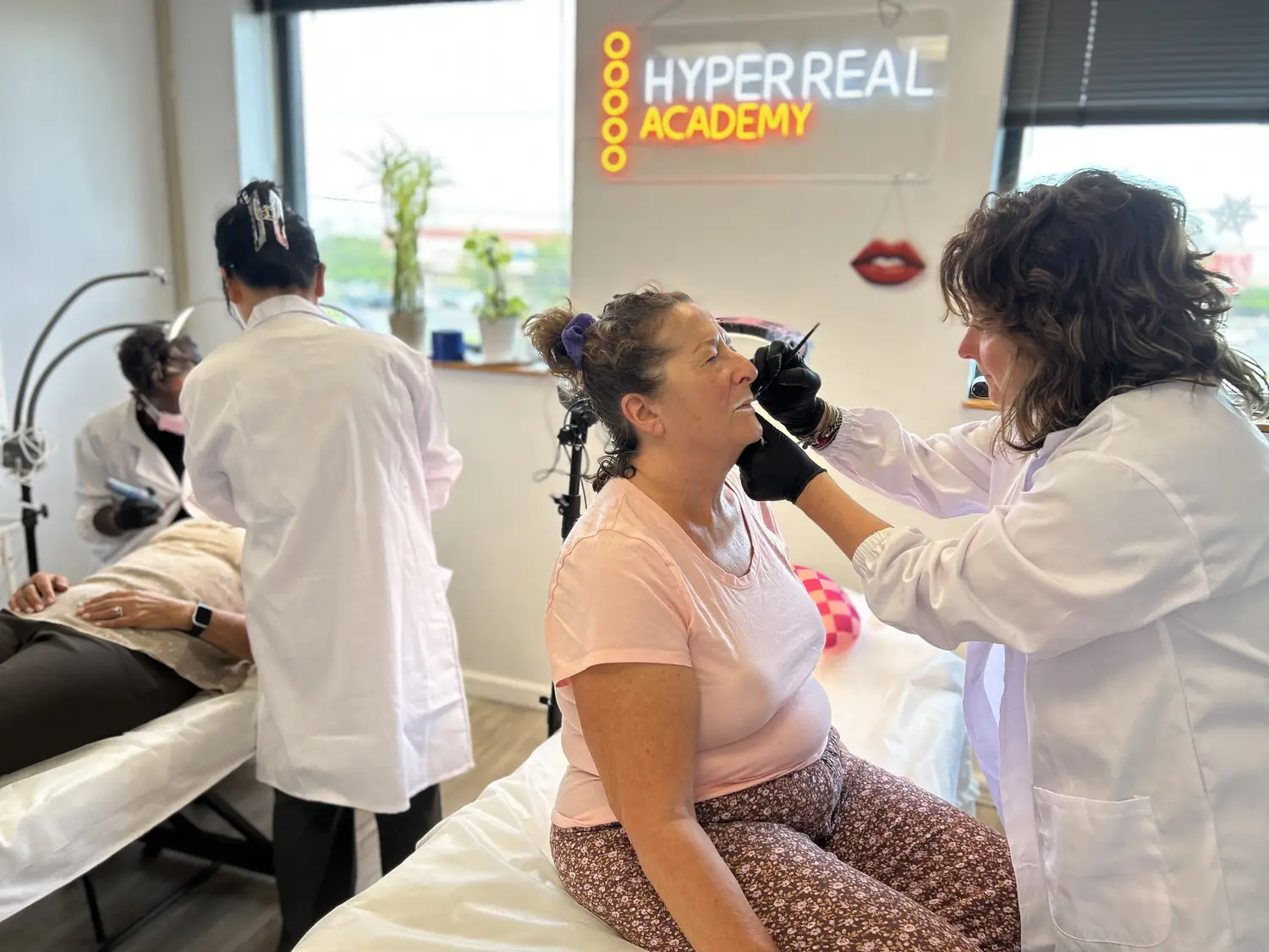 Hyper Real Academy students in lab coats perform PMU procedures on live models during a hands-on training class
