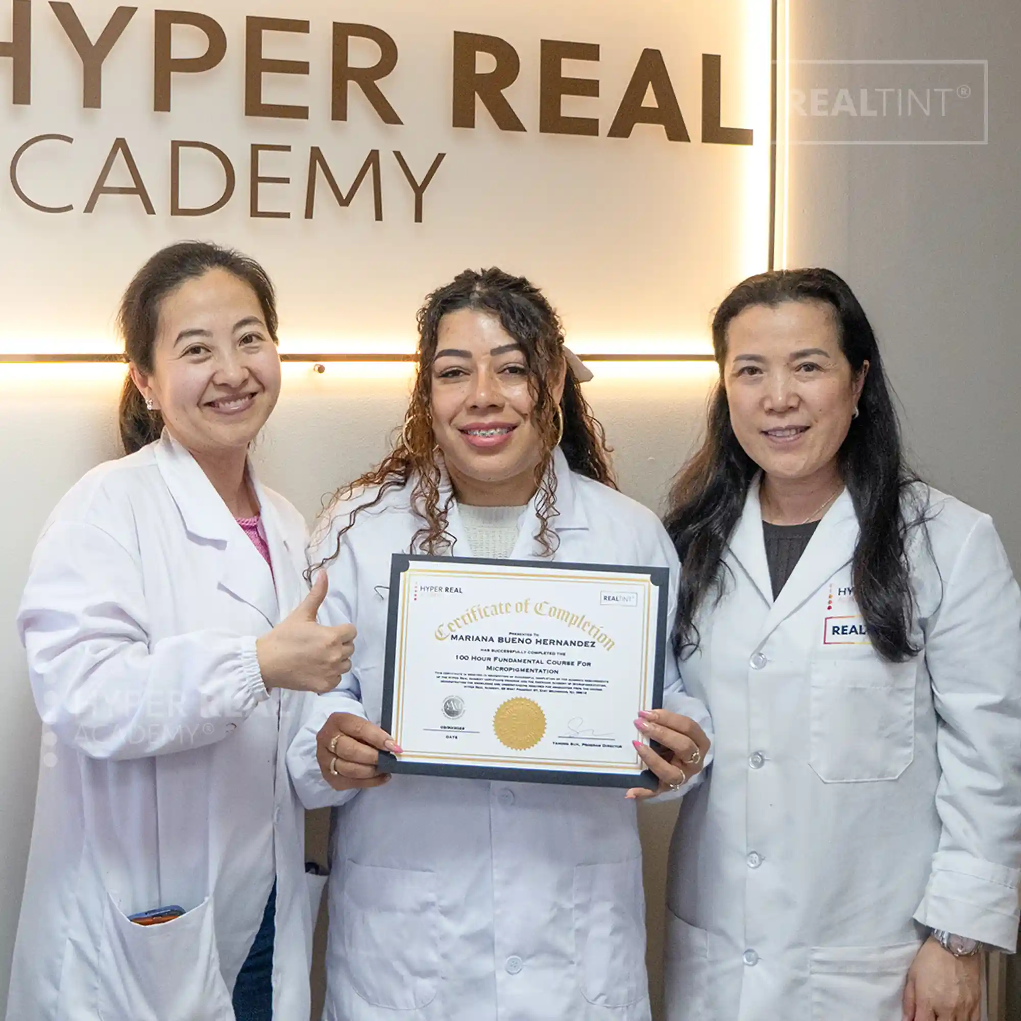 Graduate holds her 100-Hour Fundamentals certificate of completion alongside instructors at Hyper Real Academy