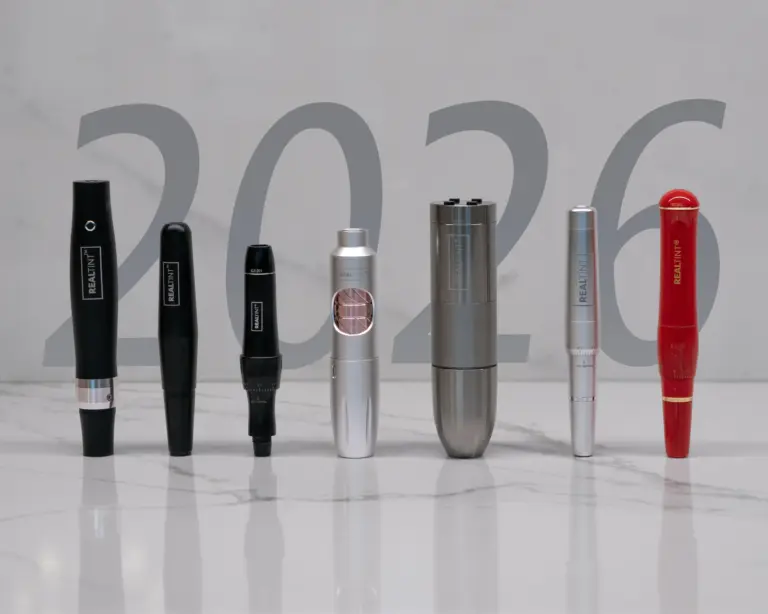 Seven RealTint(R) cordless rotary PMU pen machines in black, silver, gunmetal, and red finishes on white marble with a translucent 2026 graphic