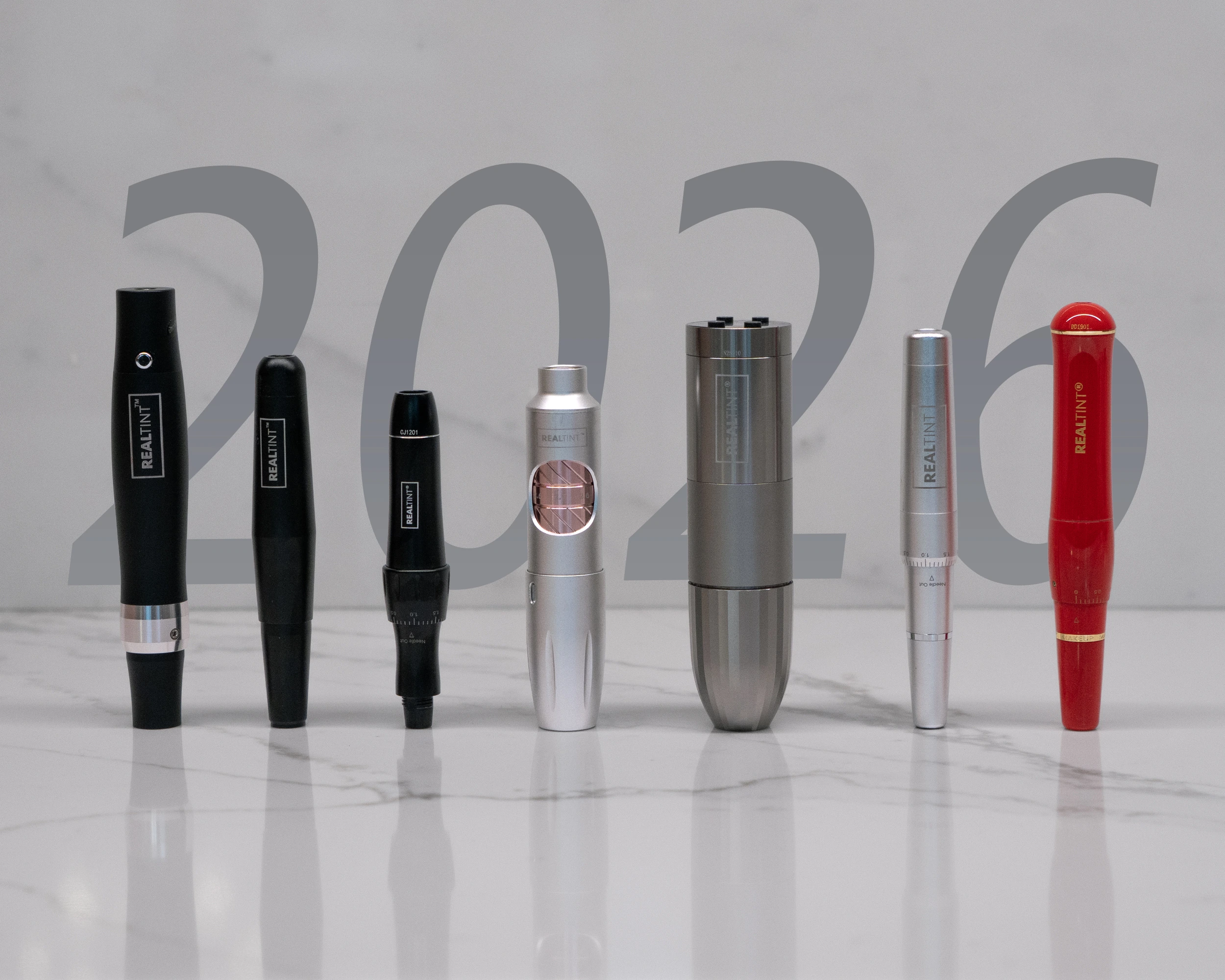 Seven RealTint(R) cordless rotary PMU pen machines in black, silver, gunmetal, and red finishes on white marble with a translucent 2026 graphic
