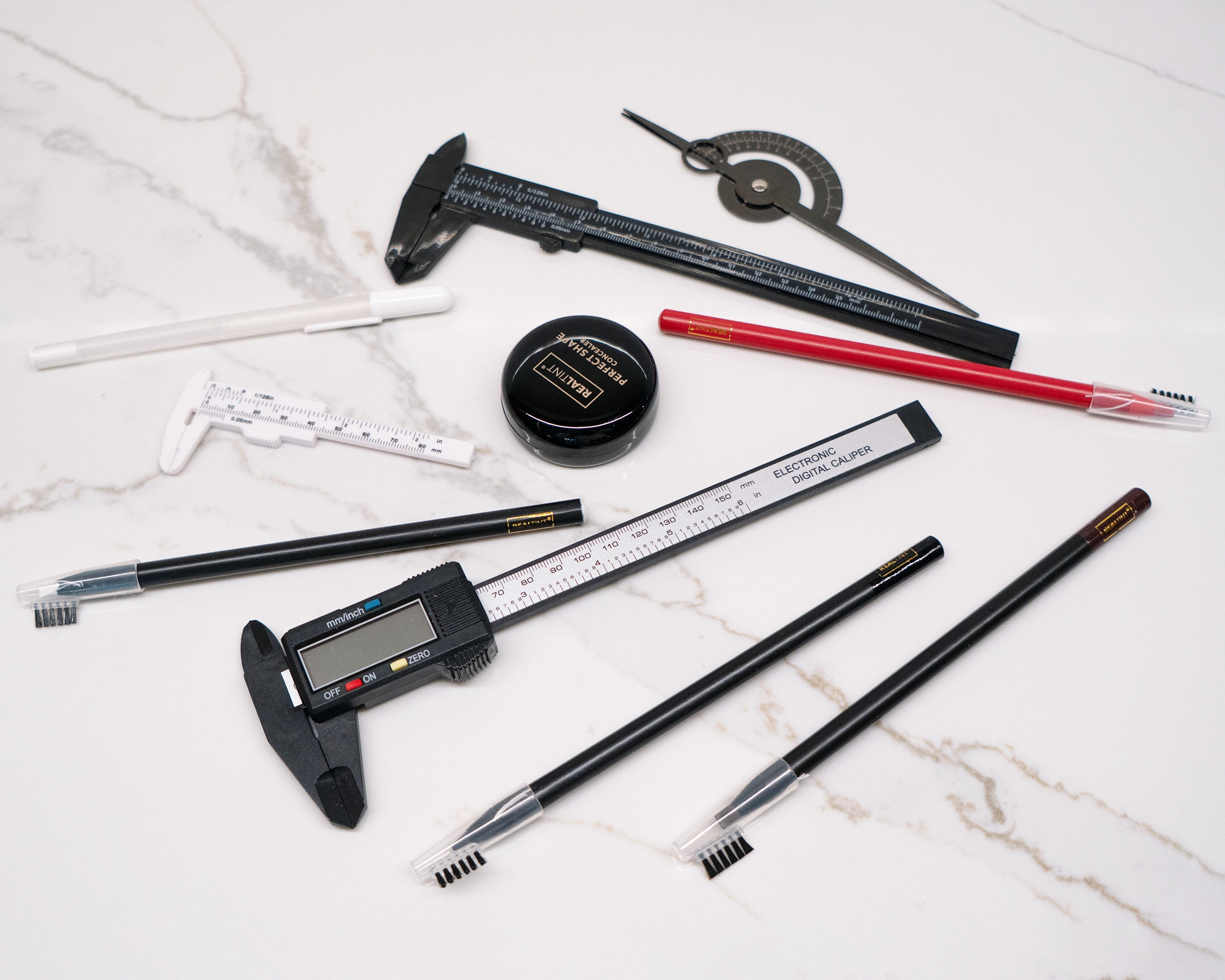 Flat lay of PMU brow-mapping tools on white marble: digital and vernier calipers, protractor angle gauge, spoolie brow pencils, and concealer for symmetry and shape mapping