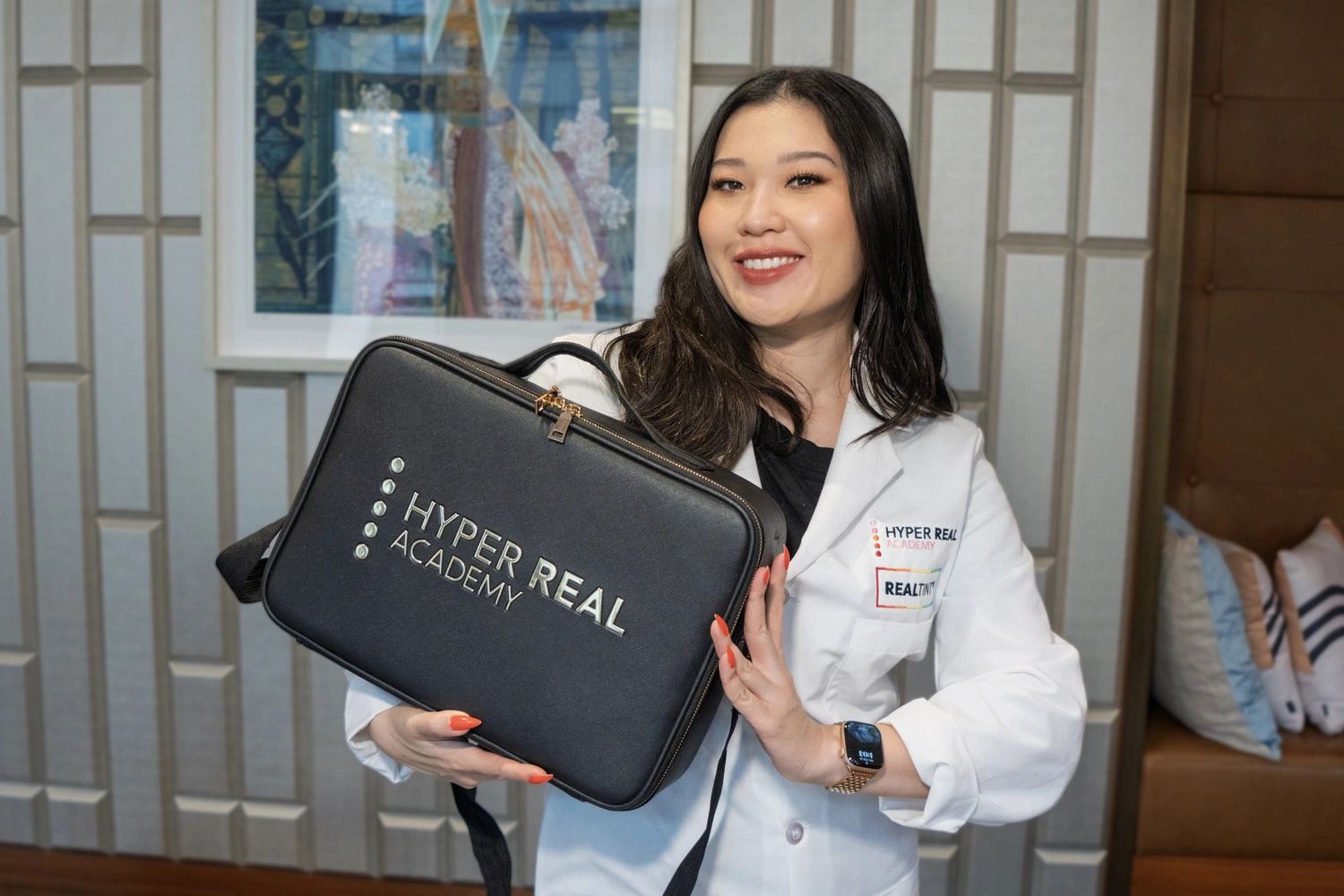 Hyper Real Academy instructor in a white lab coat holding a black branded Hyper Real Academy carrying case, a permanent makeup training and kit product shot