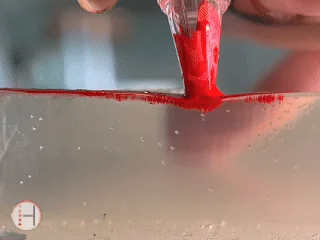 Close-up PMU training GIF: gloved fingers press saturated red lip pigment on a client to demonstrate RealTint(R) Color Blocking behavior during a Lip Blush procedure